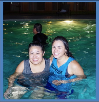 Two women pose for camera in while standing in swimming pool