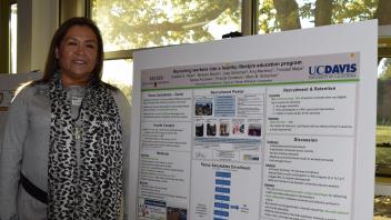 smiling woman with leopard print scarf stands next to her research poster