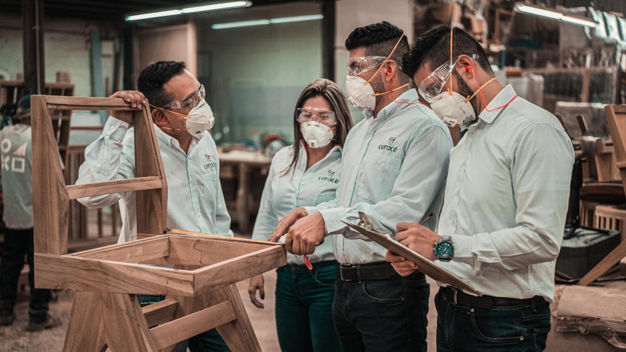 Man in denim shirt wearing a safety mask discusses work issues with associates