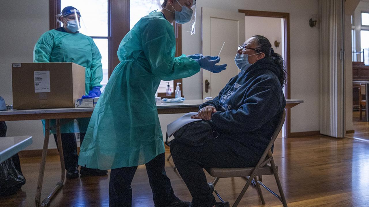 A medical provider prepares to test a woman for COVID-19 with a swab