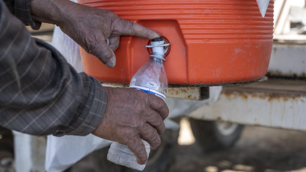 Close-up image of a farmworker's hands dispensing water into a water bottle.