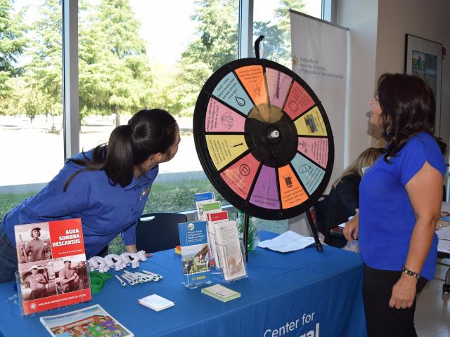 WCAHS Outreach worker play the spin the wheel game with a member of the public visiting the outreach table at an event