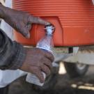 Close-up image of a farmworker's hands dispensing water into a water bottle.